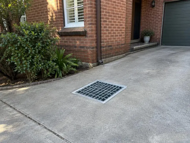 Clean outdoor drain grate in a concrete driveway beside a brick house in Bellevue Hill