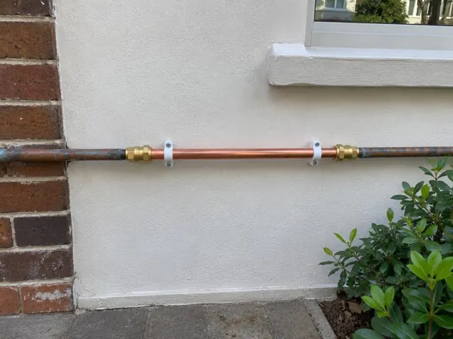 Exterior wall with a newly repaired copper water pipe section between older pipes in Double Bay