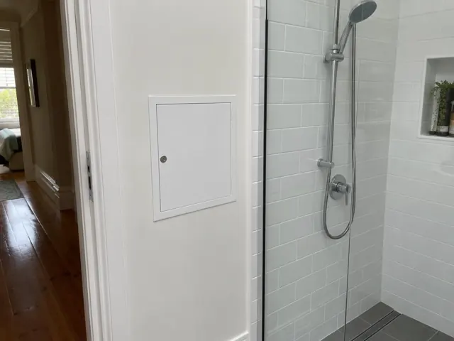 Small white access panel on a painted hallway wall beside a tiled shower in a home in Paddington